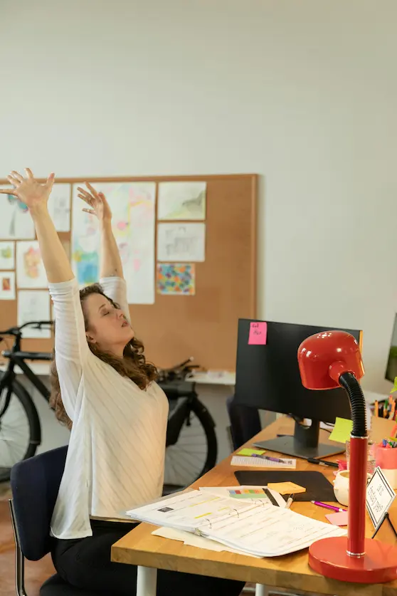 Woman stretching on office chair in front of desk and computer to support spine health at work and home