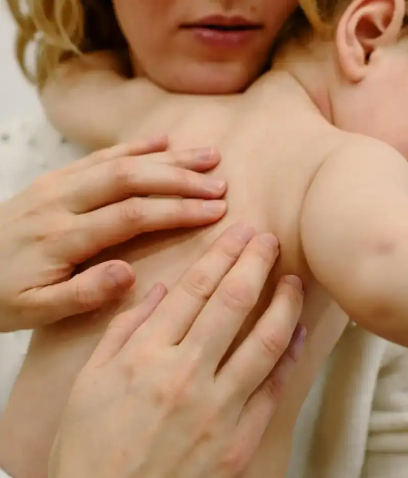 Chiropractor examining a baby’s spine while being held by mother, in a caring clinic environment.