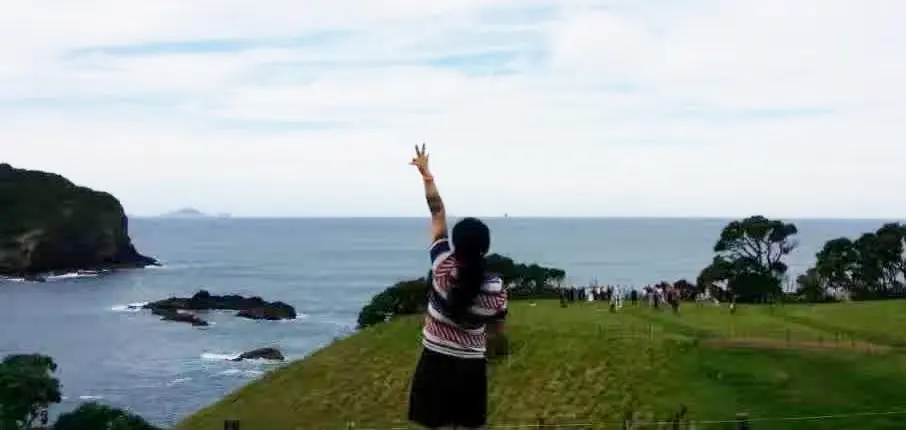 Dr Angel Lu standing by the shoreline, holding up a peace sign to the sky, symbolizing commitment as a Justice of the Peace