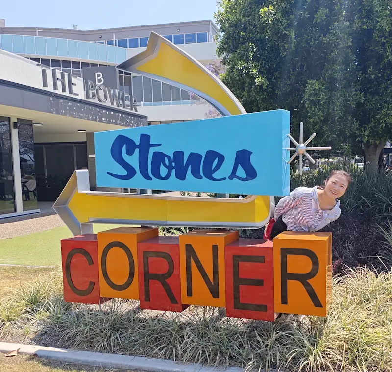 Dr Angel from Angel Chiropractic standing behind the Stones Corner suburb sign, representing her dedication to caring for the local community.
