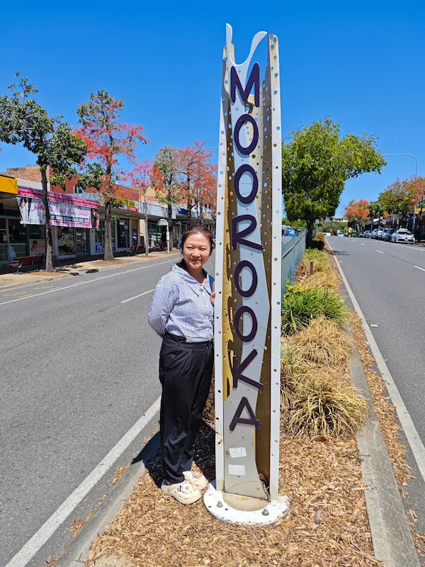Dr Angel from Angel Chiropractic standing beside the Moorooka suburb sign, representing local chiropractic services for Moorooka residents.