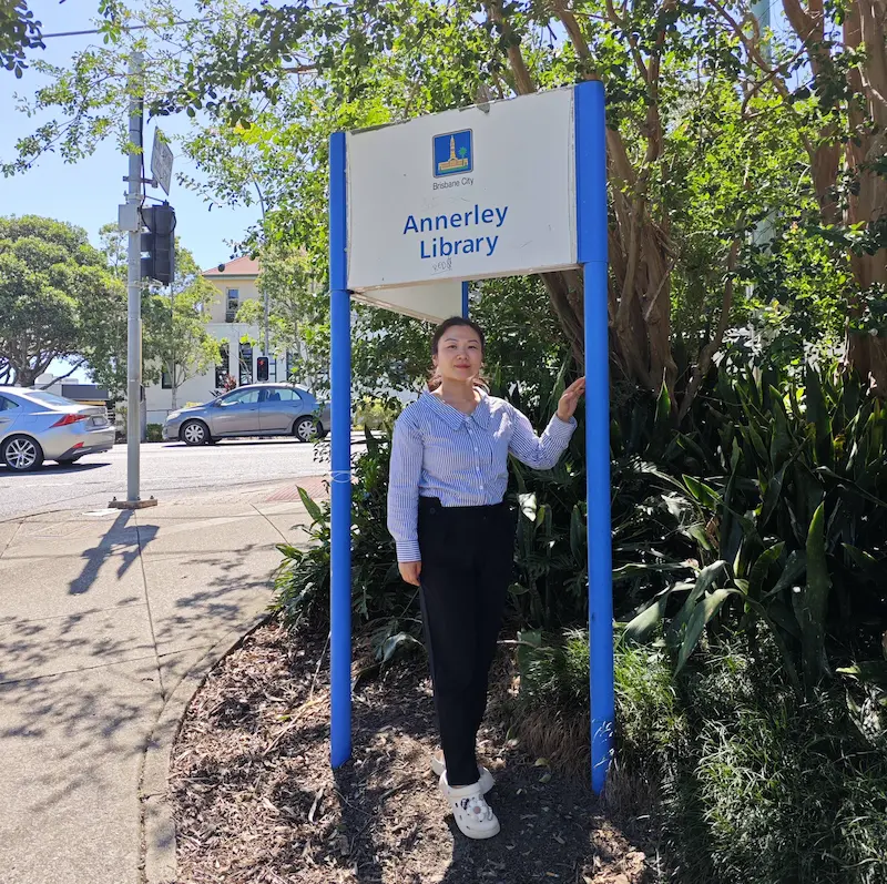 Dr Angel from Angel Chiropractic standing under the Annerley Library sign, representing local chiropractic care in Annerley Brisbane.