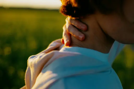 Woman holding her neck in pain outdoors under sunlight, representing knot in neck relief at Angel Chiropractic Brisbane